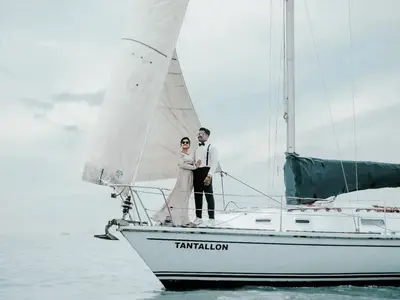 A couple in formal wear on the bow of Tantallon under sail, her name on the hull