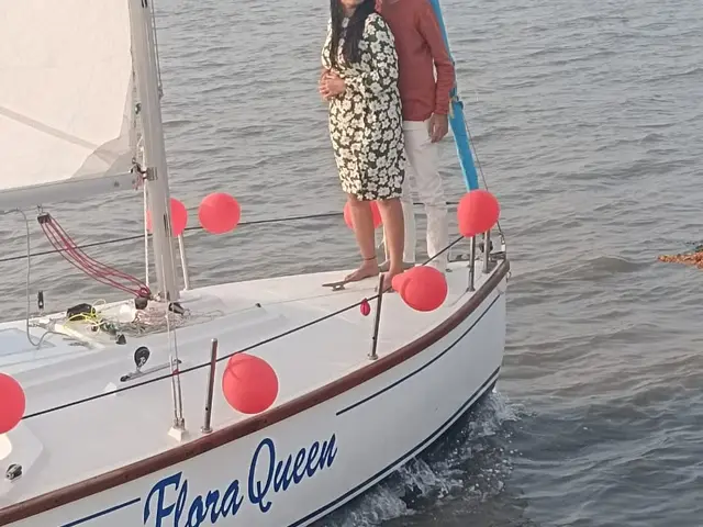 A couple posing at the bow of the sailboat Flora Queen with the Mumbai skyline behind